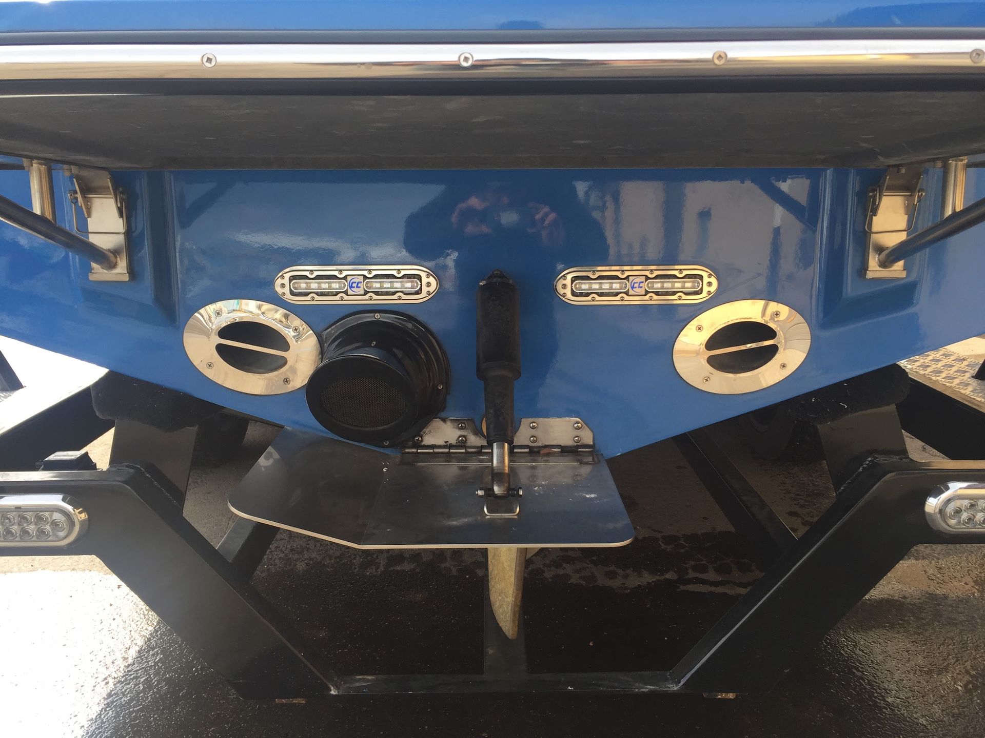 Close-up of a blue boat stern with black hardware and circular vents in bright sunlight