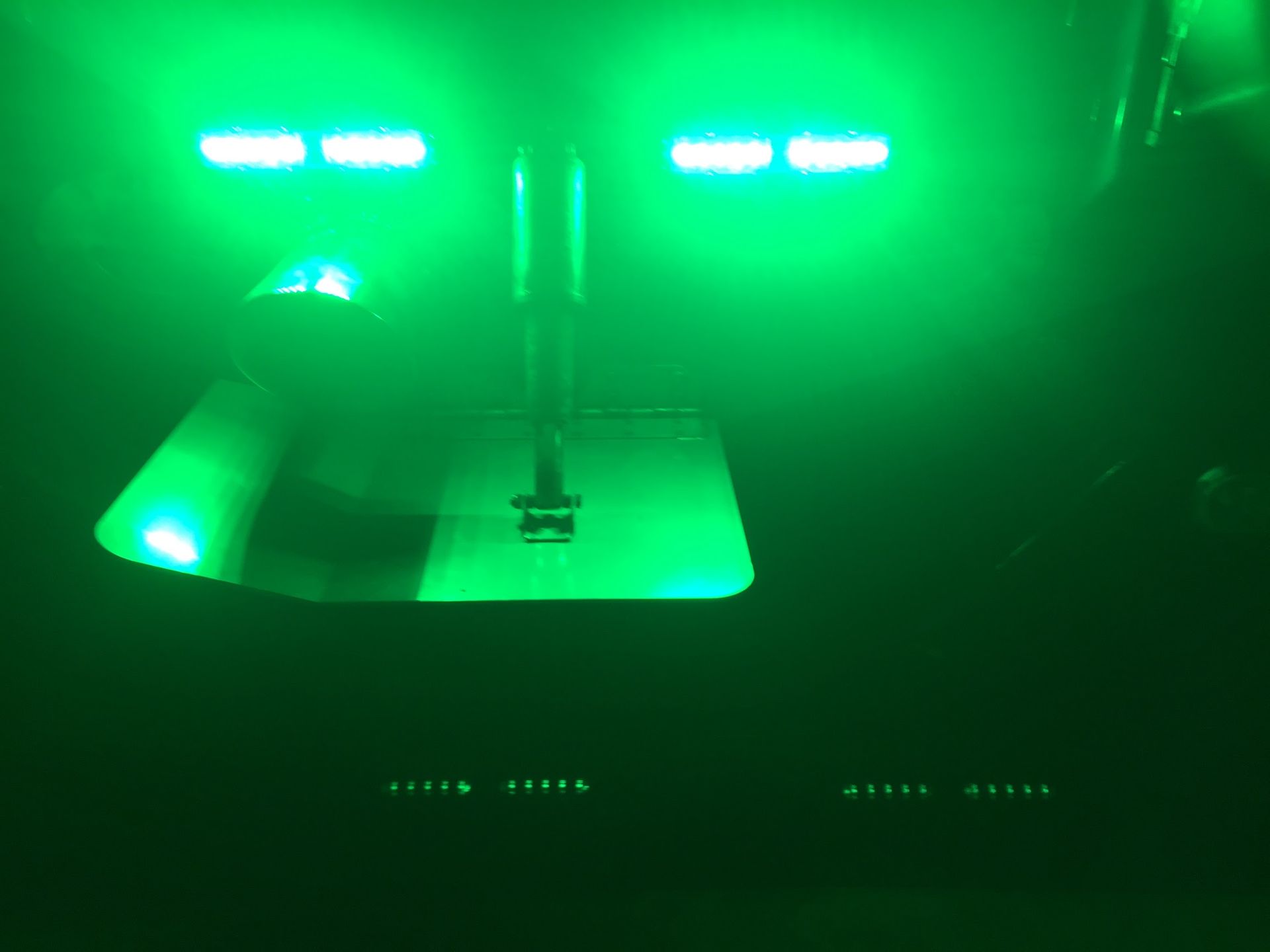 Green-lit indoor room with a bed and bright light bars on the wall and ceiling