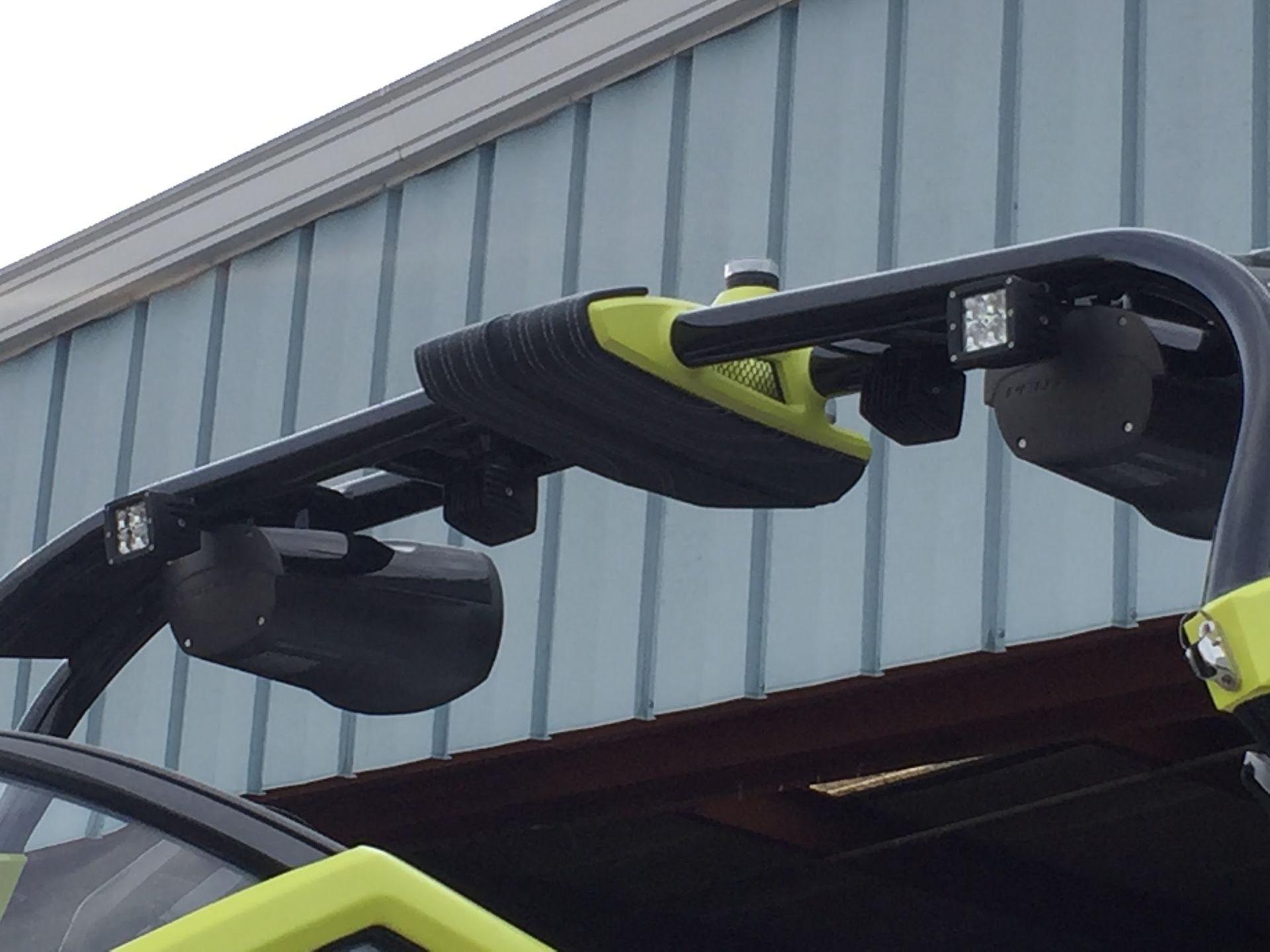 Close-up of a car's roof-mounted bike rack with black and lime-green arms against a building.