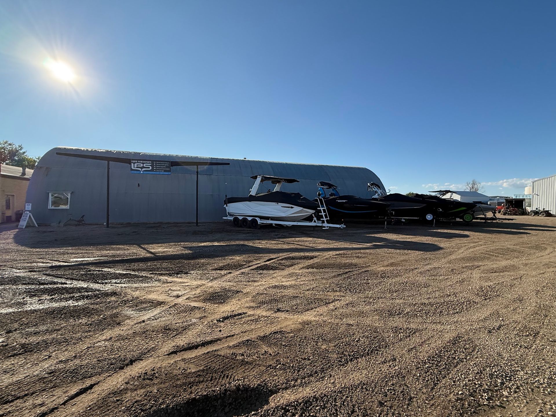 Helicopter parked beside a long gray hangar on a dusty airfield under a bright blue sky