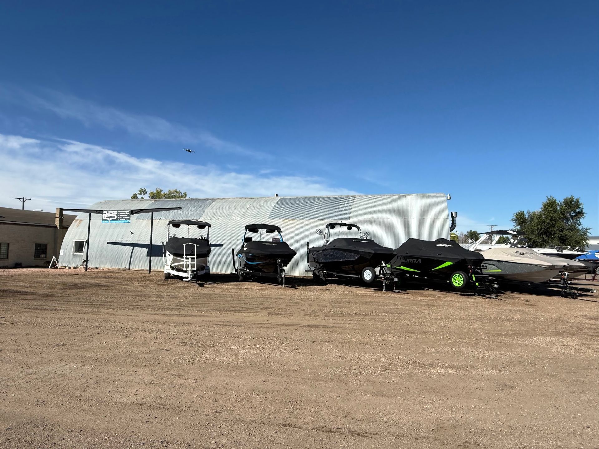 Parked black and green ATVs beside a white metal building in a dusty lot under a blue sky