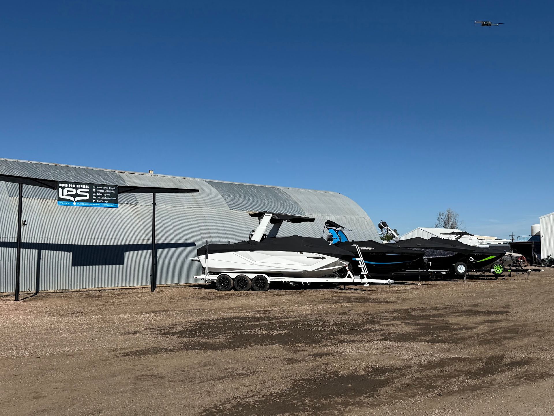 Small airplanes parked beside a corrugated metal hangar on a dirt airfield under a clear blue sky