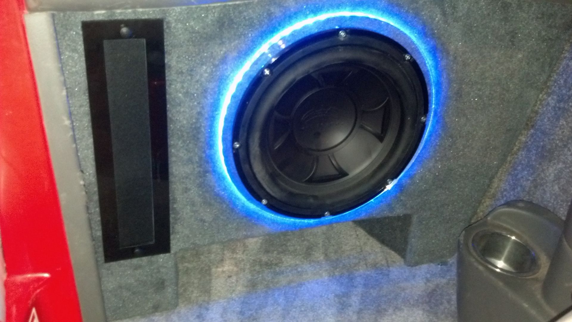 Car audio subwoofer with blue LED ring beside a rectangular speaker grille