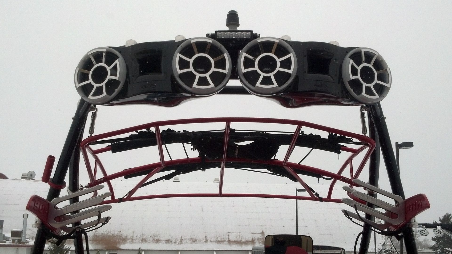 Rear view of a vehicle with four roof-mounted round speakers and red roll cage bars under a gray sky