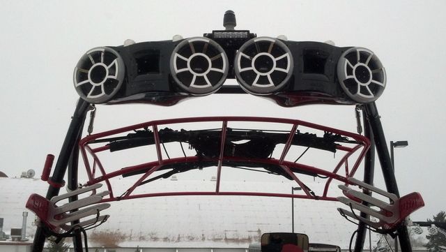 Rear view of a red off-road vehicle with four roof-mounted lights against a cloudy sky