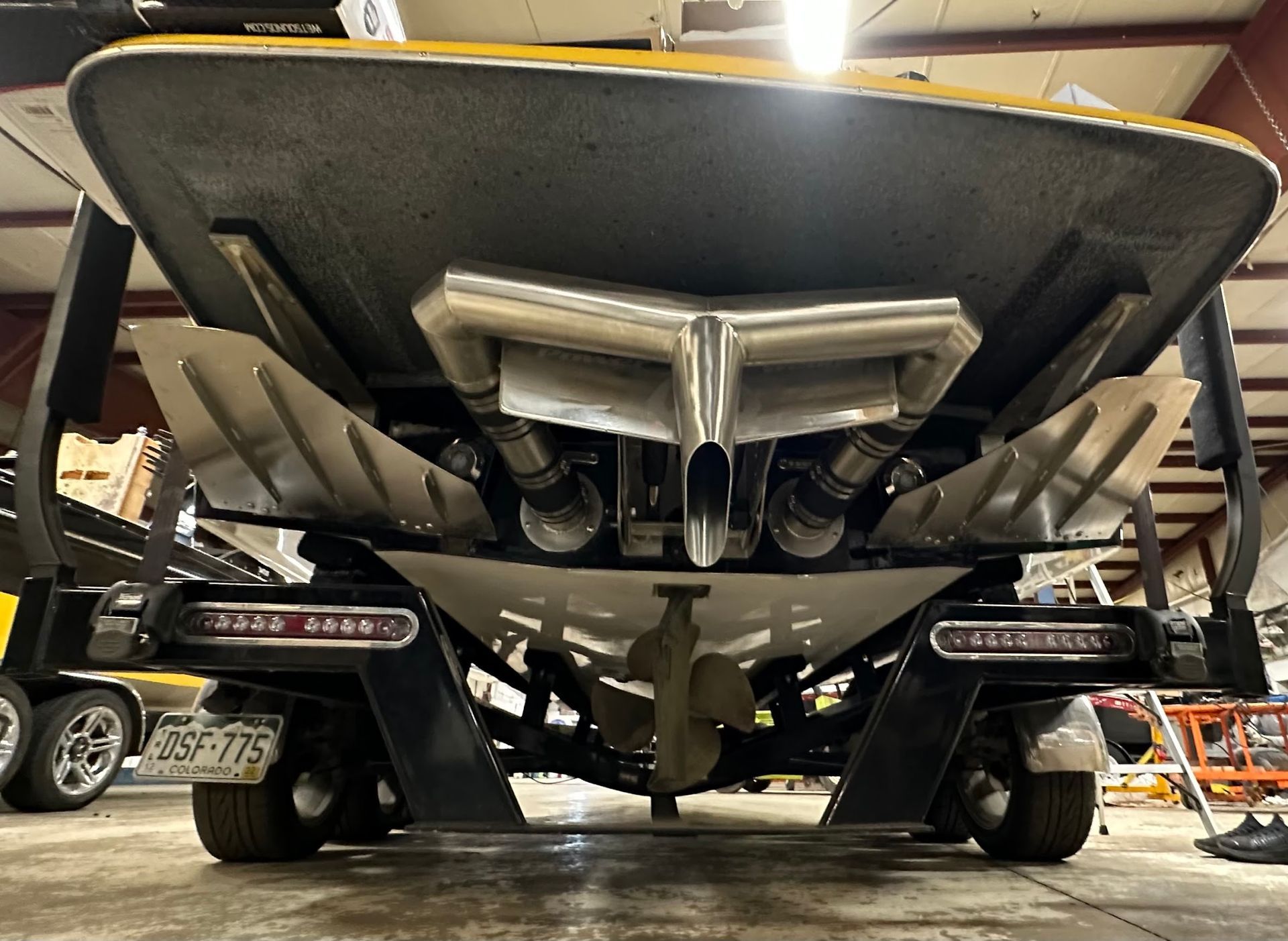 Rear view of a black speedboat on a trailer in a workshop, showing twin propellers and undercarriage.