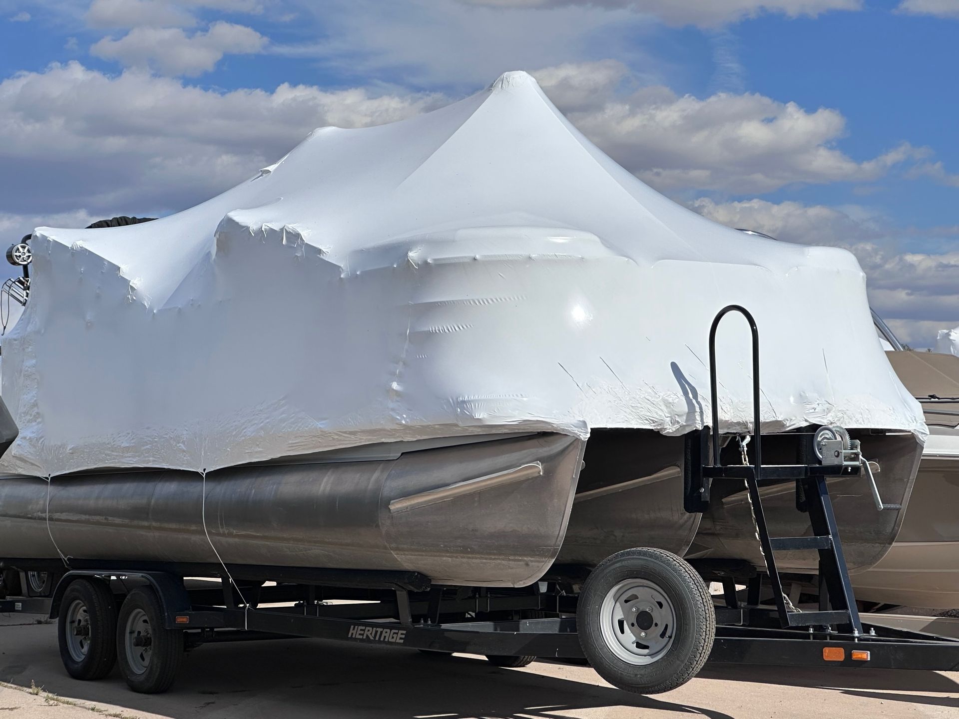 Boat wrapped in white shrink wrap on a trailer, parked outdoors under a cloudy sky.
