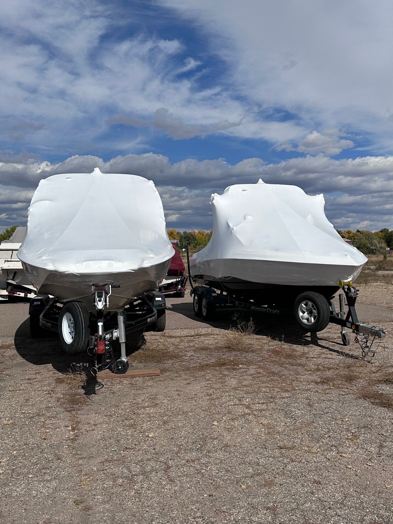 Two boats wrapped in white covers parked on trailers under a cloudy sky.