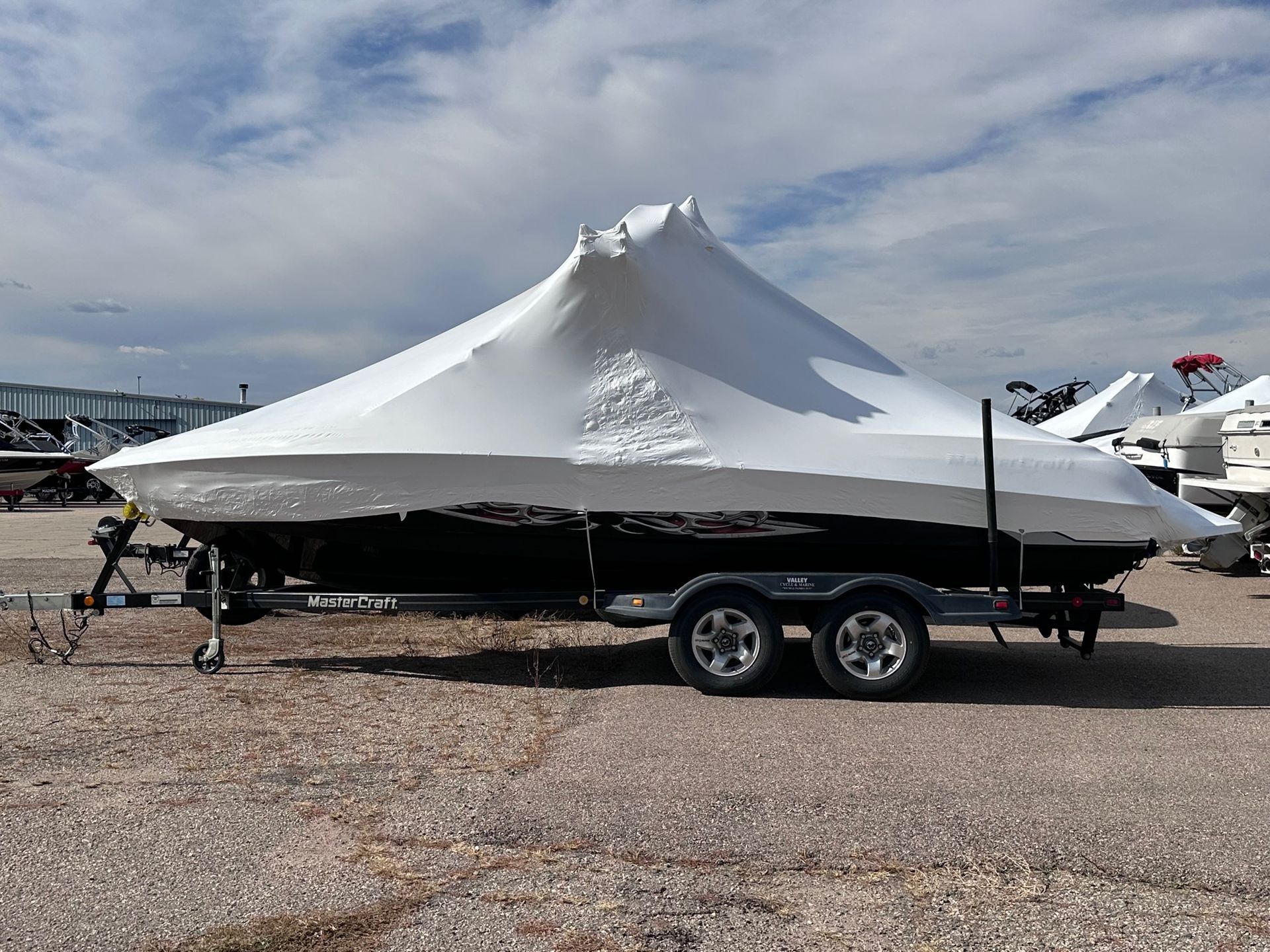 Snow-covered boat on a trailer in a gravel lot under a cloudy sky