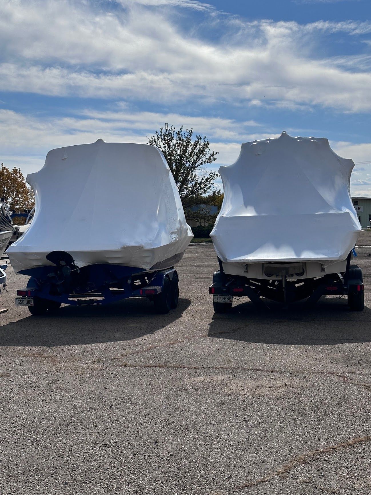 Two cars in a parking lot covered with white protective covers under a cloudy sky.