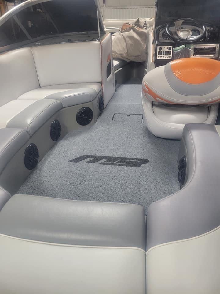 Boat interior with gray-and-white seating, carpeted floor, speakers, and an orange-and-gray cushion