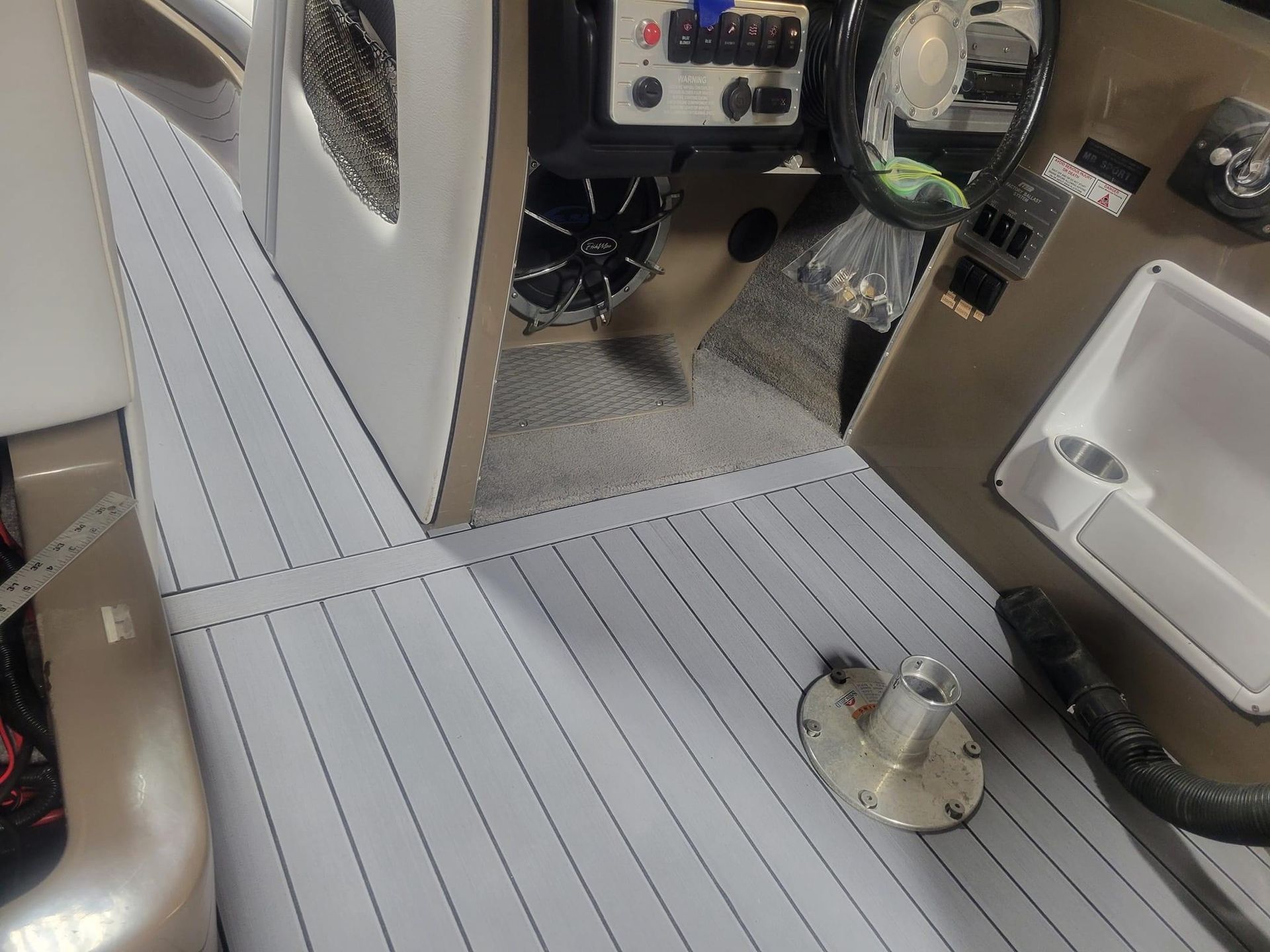 Boat cabin interior with gray vinyl flooring, helm console, and side door opening to the deck.