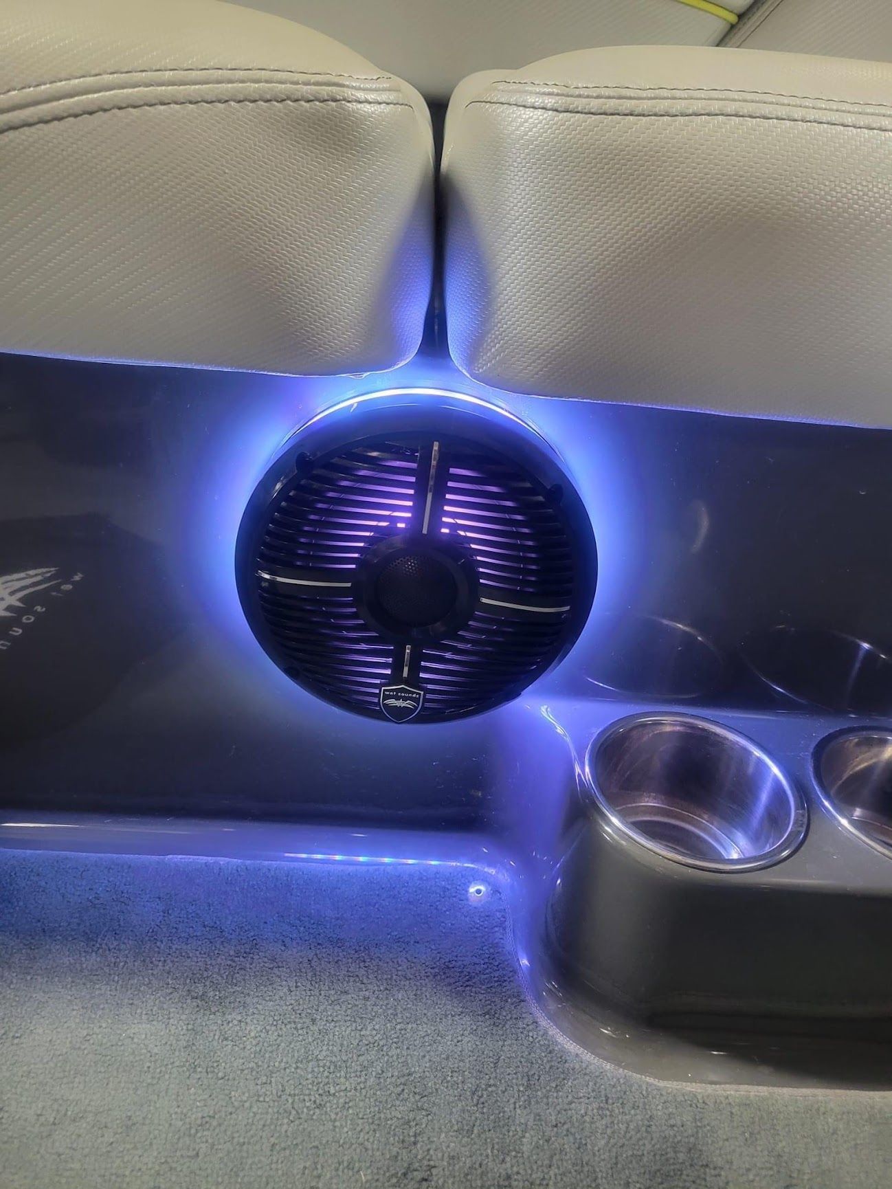 Purple LED-lit speaker between beige seats with cupholders nearby