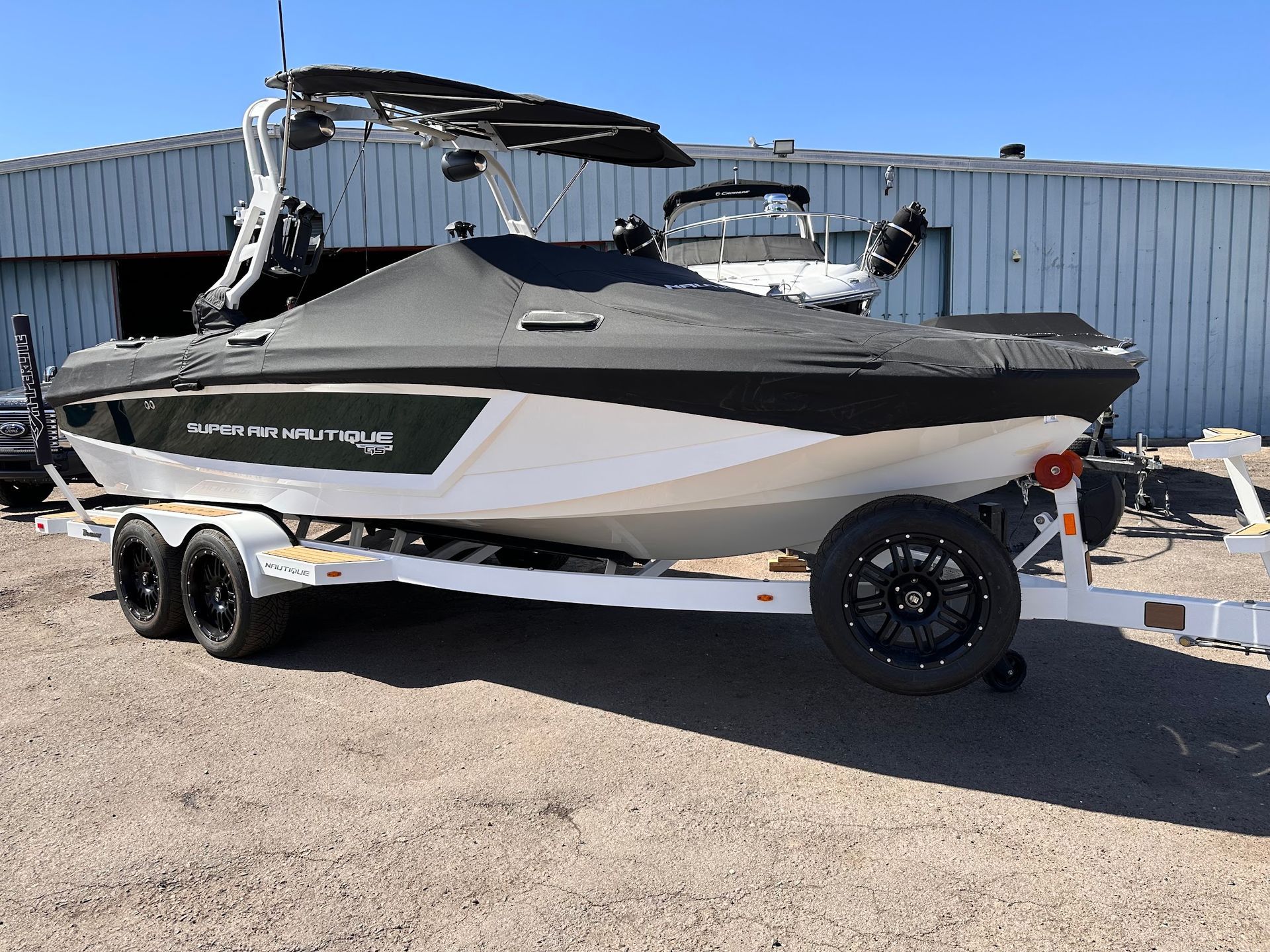 White and black speedboat on a trailer parked on gravel beside a corrugated metal building