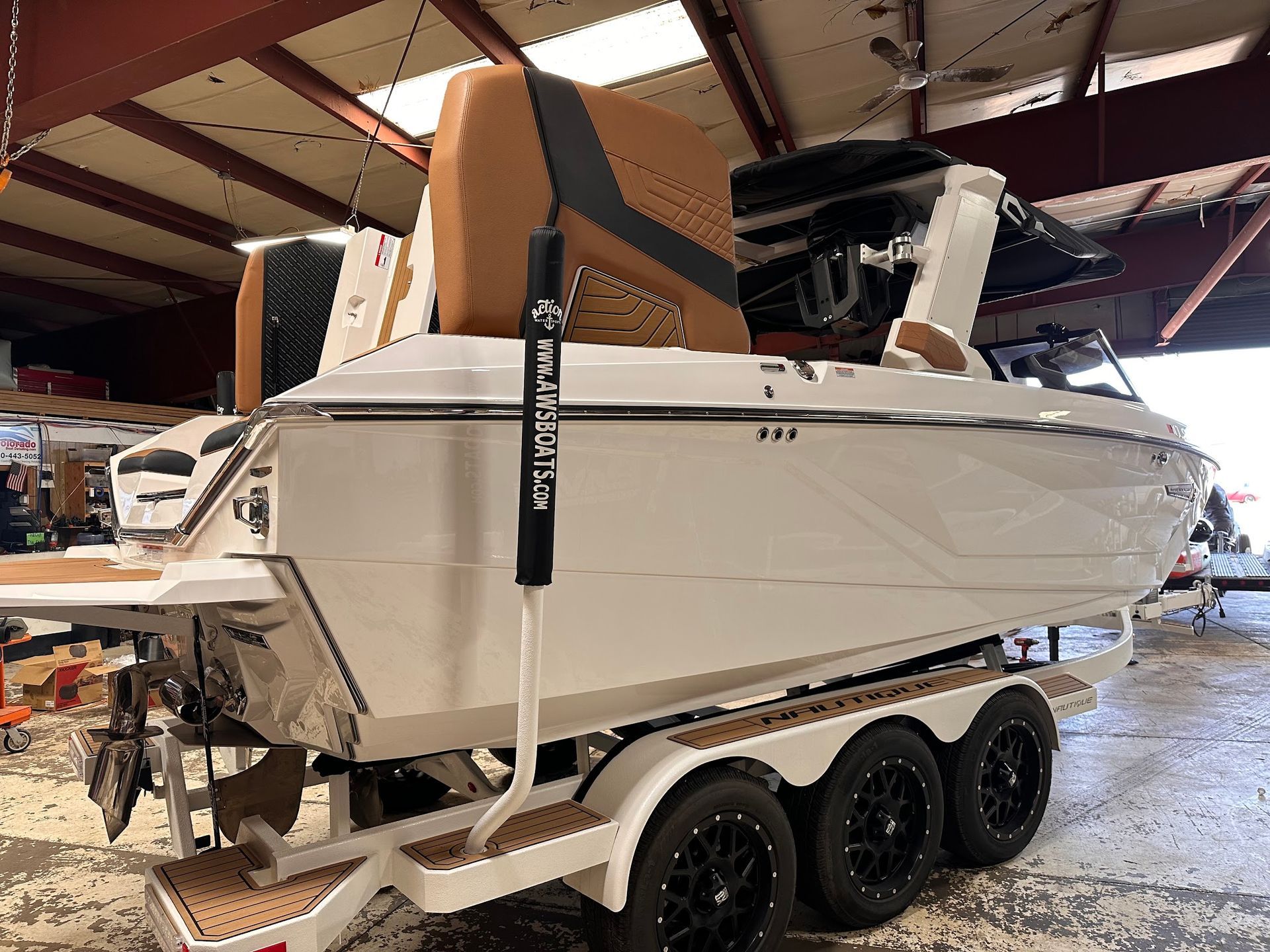 White boat on a triple-axle trailer inside a warehouse, with a tan cover and support straps.