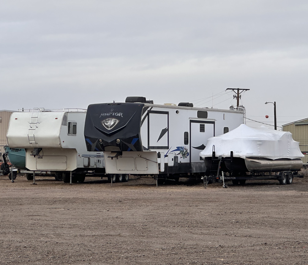 Two RVs parked in a lot under an overcast sky, one with a snow-covered trailer