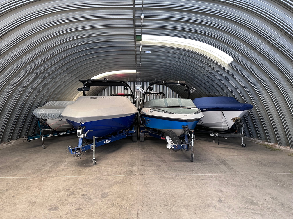 Three small boats parked inside a corrugated metal storage shed