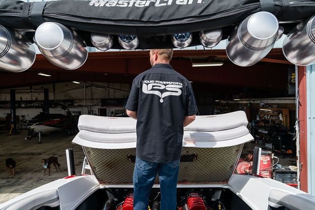 Person standing at the rear of a white MasterCraft boat in a garage, viewed from behind