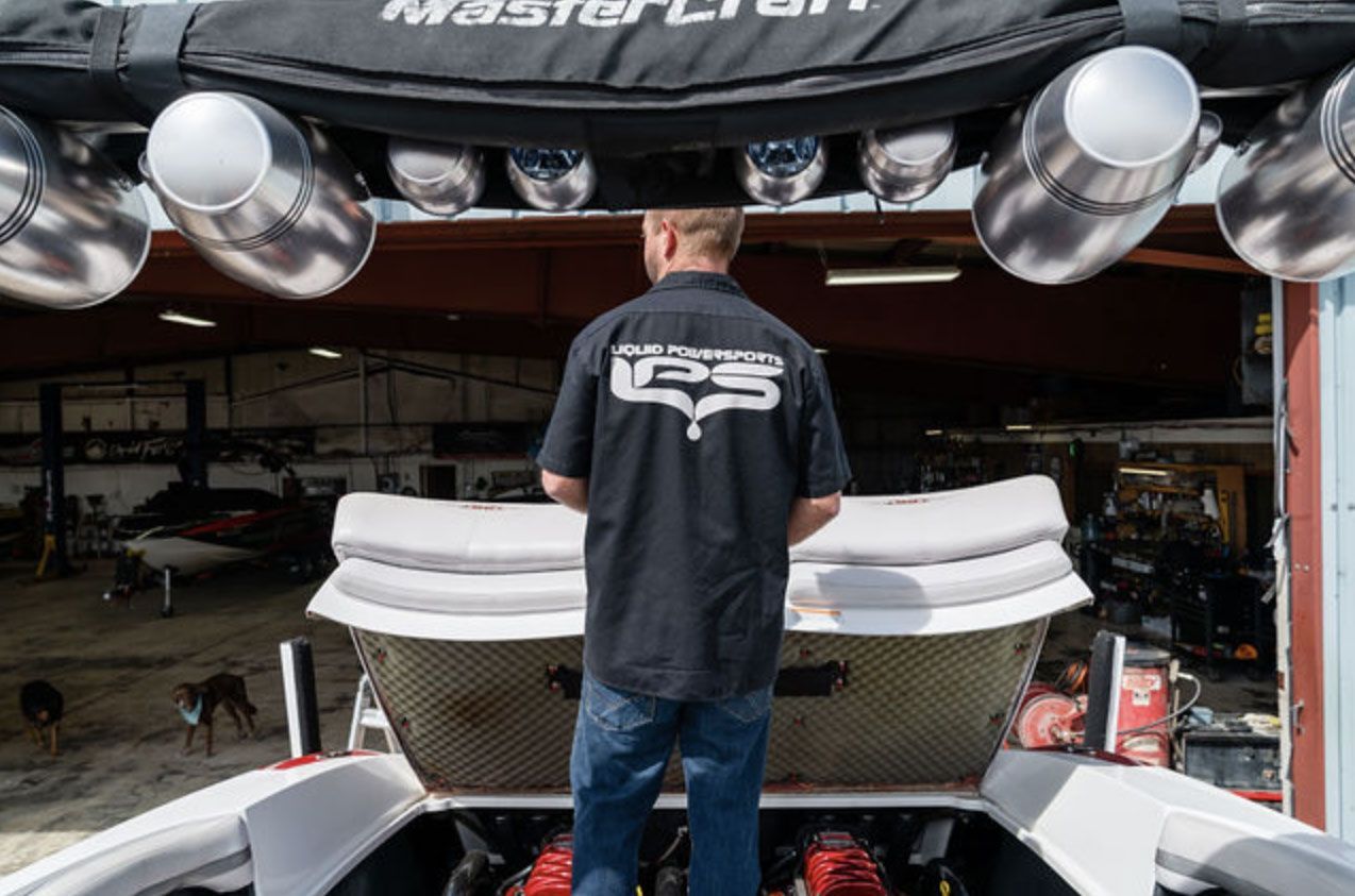Person in black shirt standing behind a race car in a garage, with large silver speakers overhead