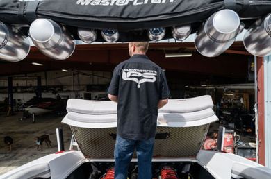 Person in black shirt standing behind a race car in a garage, with large silver speakers overhead