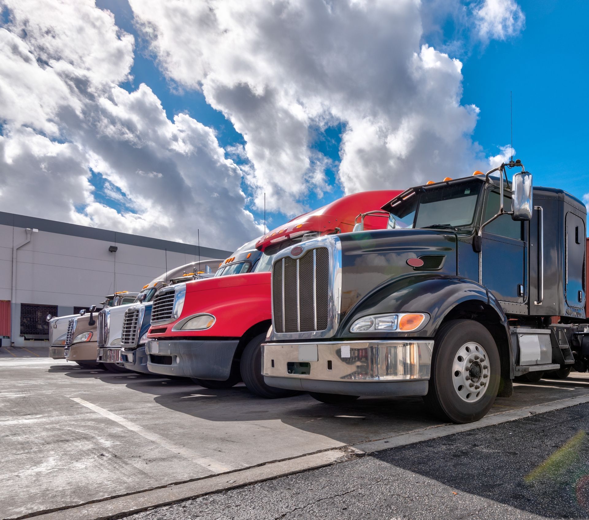 Semi trucks parked in a lot under a cloudy blue sky