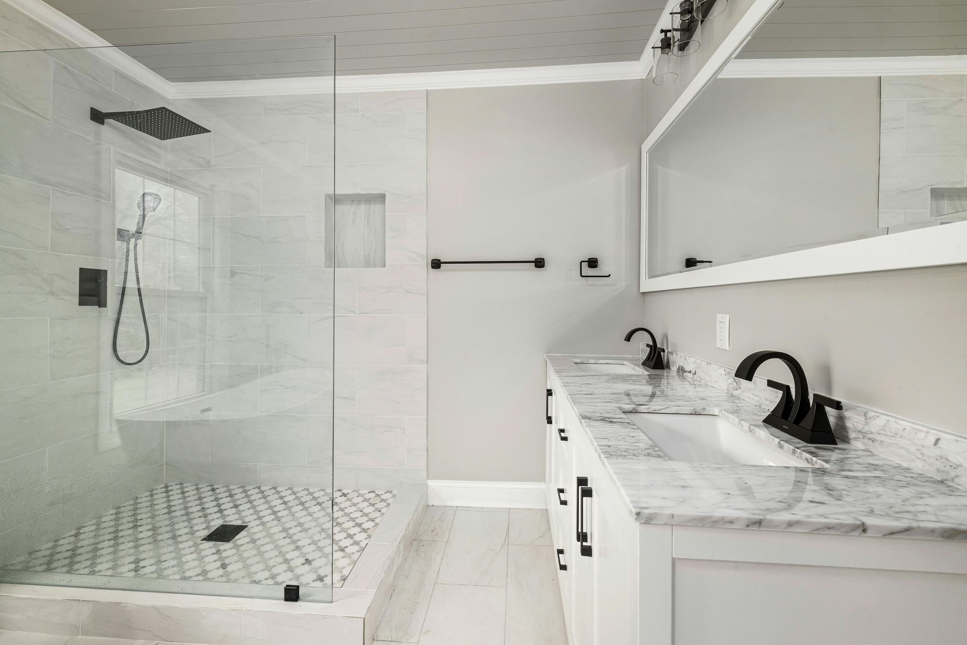 White marble countertops on a double vanity with dark fixtures and an open glass shower.