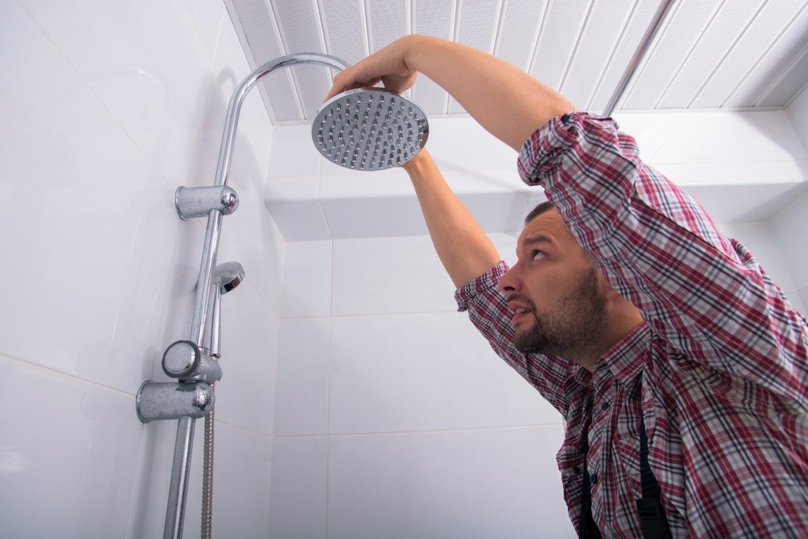 A male worker in a plaid shirt installing a shower head in a white shower