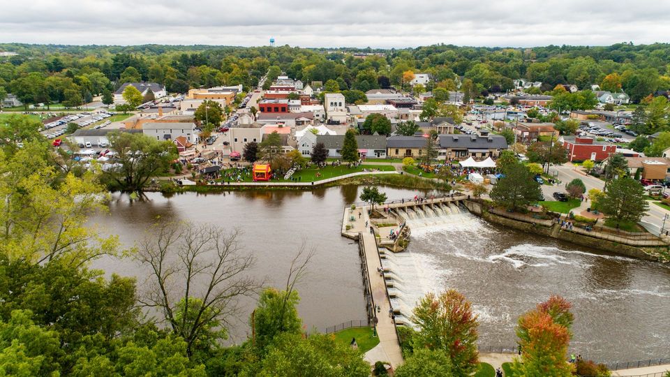 Aerial view of a town along a river with a dam; cloudy day; trees and buildings visible.