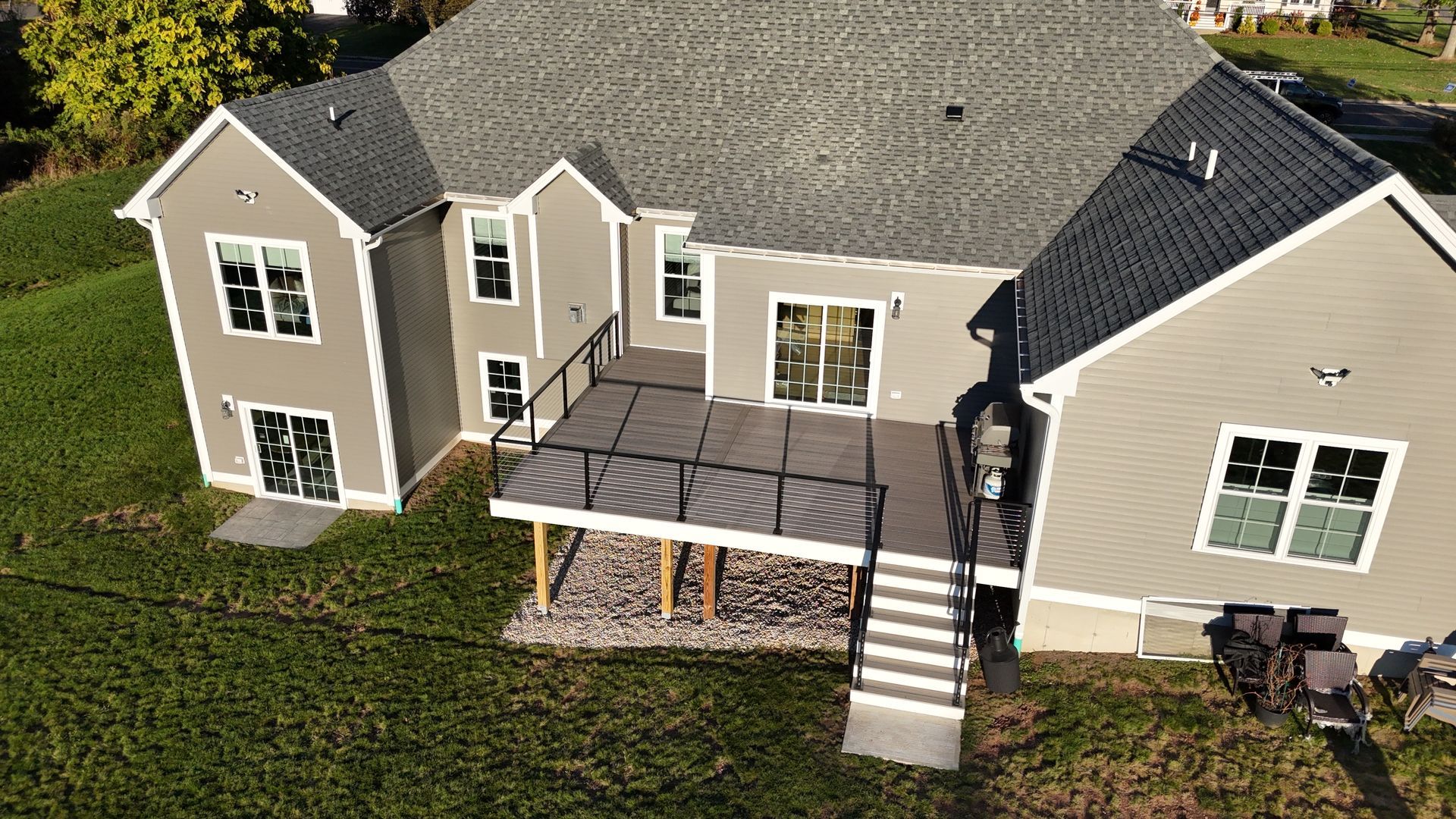 Aerial view of a gray house with a deck and stairs, on a green lawn.