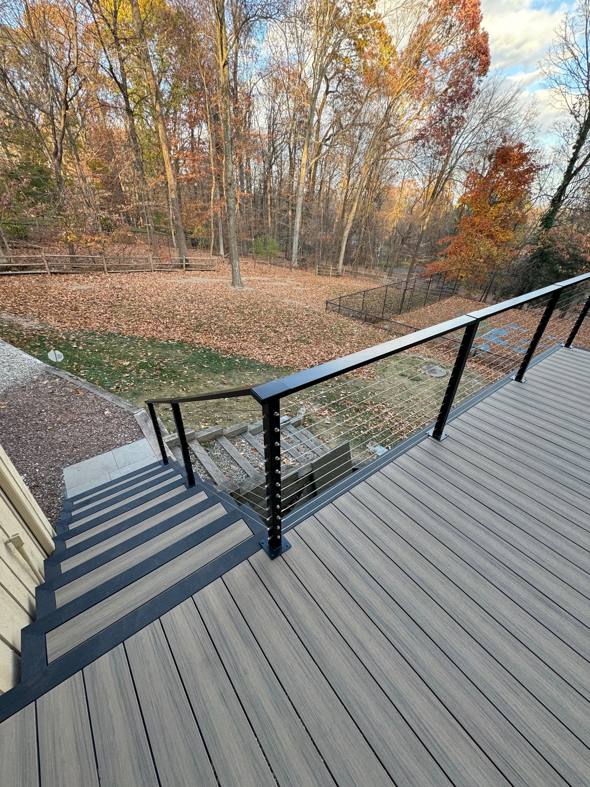 A wooden deck with stairs leading up to it and a glass railing.