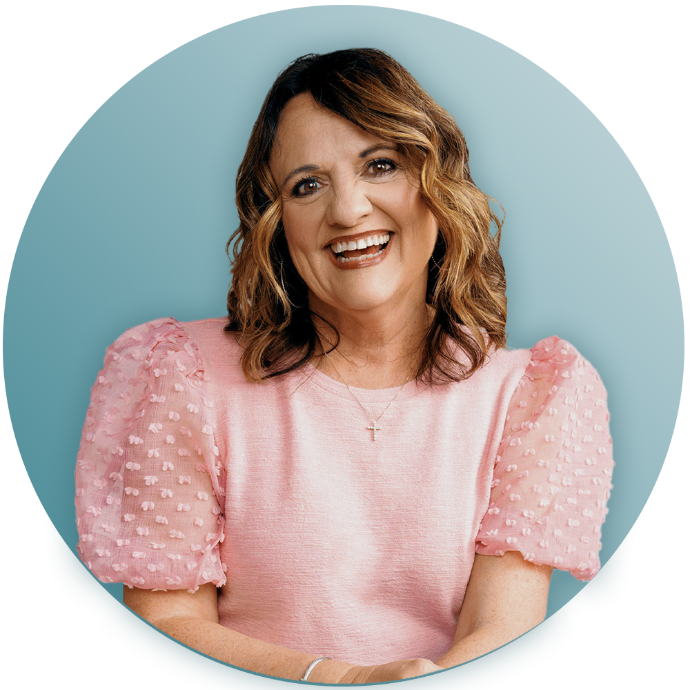 A woman in a pink sweater is smiling and wearing a cross necklace.