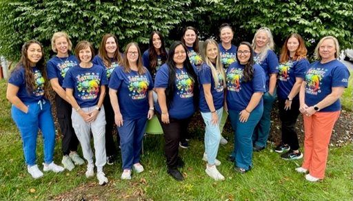 Group of people in matching blue shirts posing outdoors on grass in front of greenery.