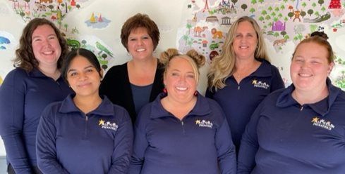 Seven staff members in navy polo shirts smiling in front of a colorful wall mural.