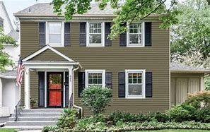 A house with a red door and black shutters is sitting on top of a lush green lawn.