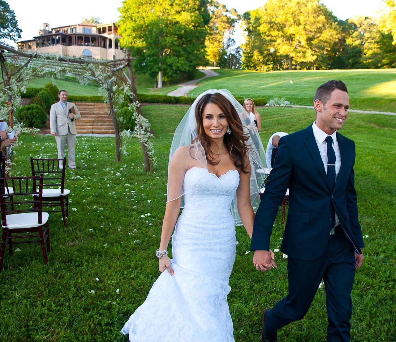 Bride and groom walking hand in hand on a garden lawn at an outdoor wedding venue.
