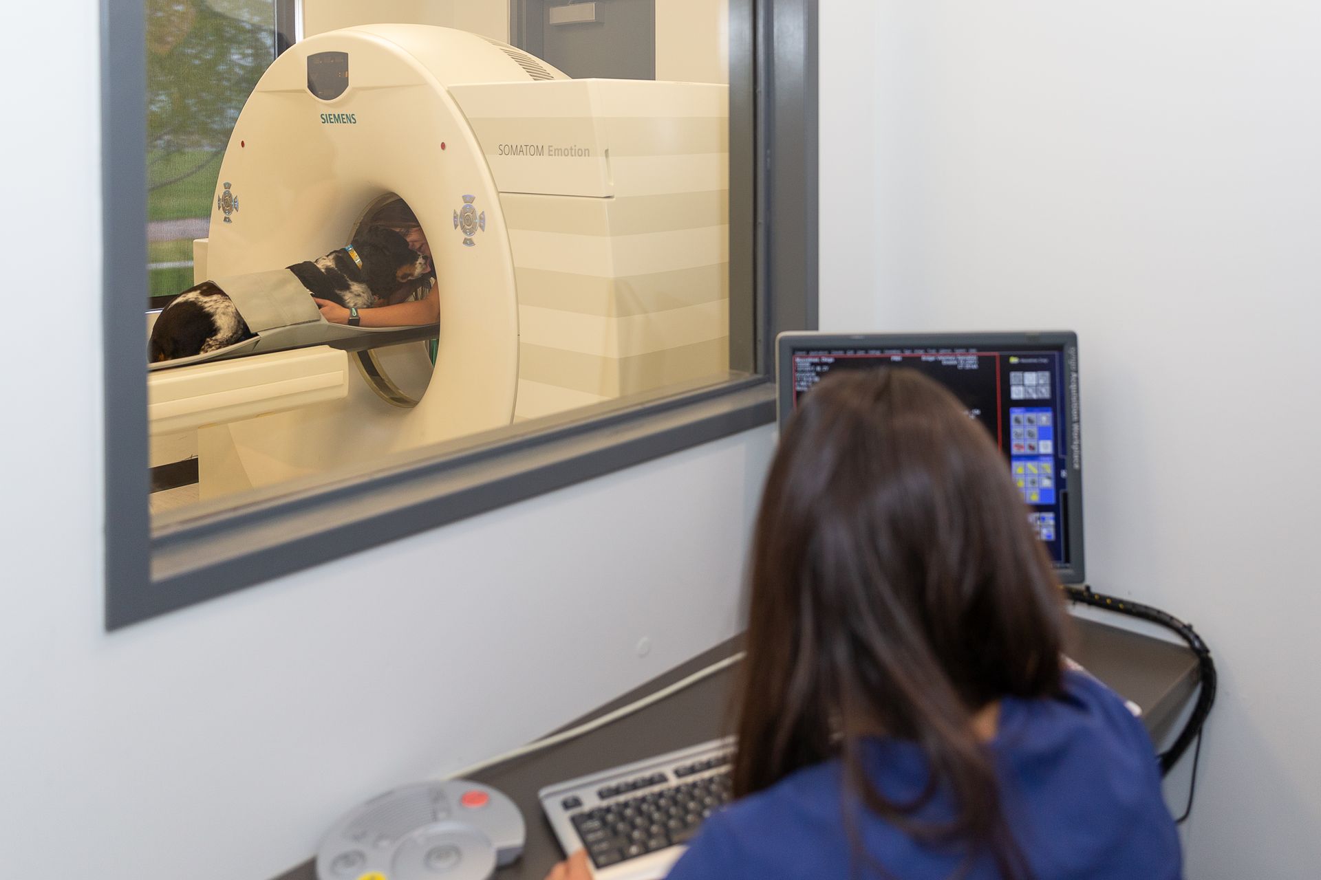 Technician at a computer monitoring a patient in an MRI scanner through a control-room window