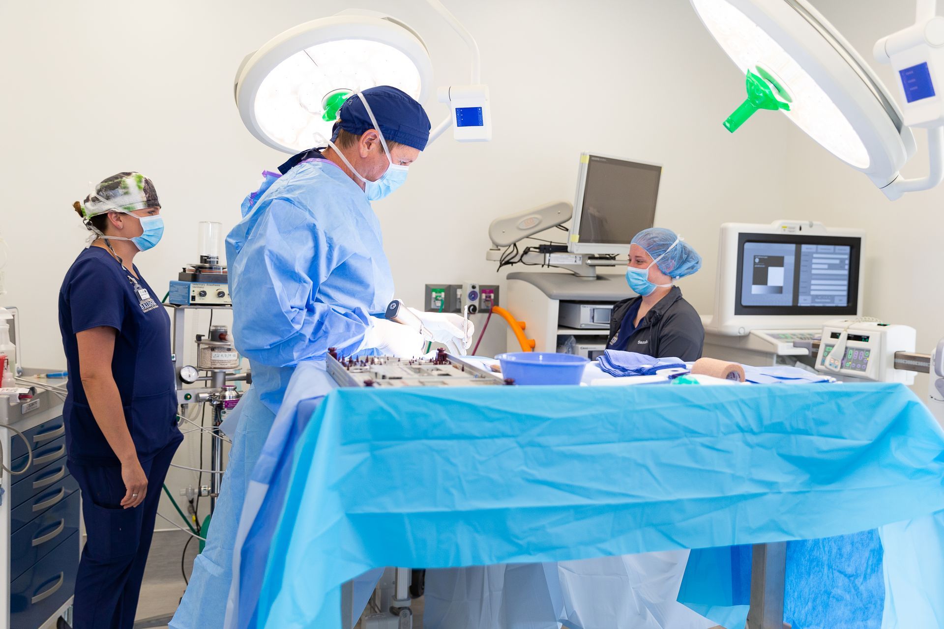 Medical team in blue scrubs in an operating room, preparing a patient under bright surgical lights.