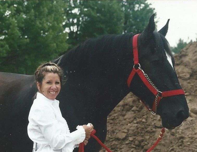 A woman standing next to a black horse with a red bridle