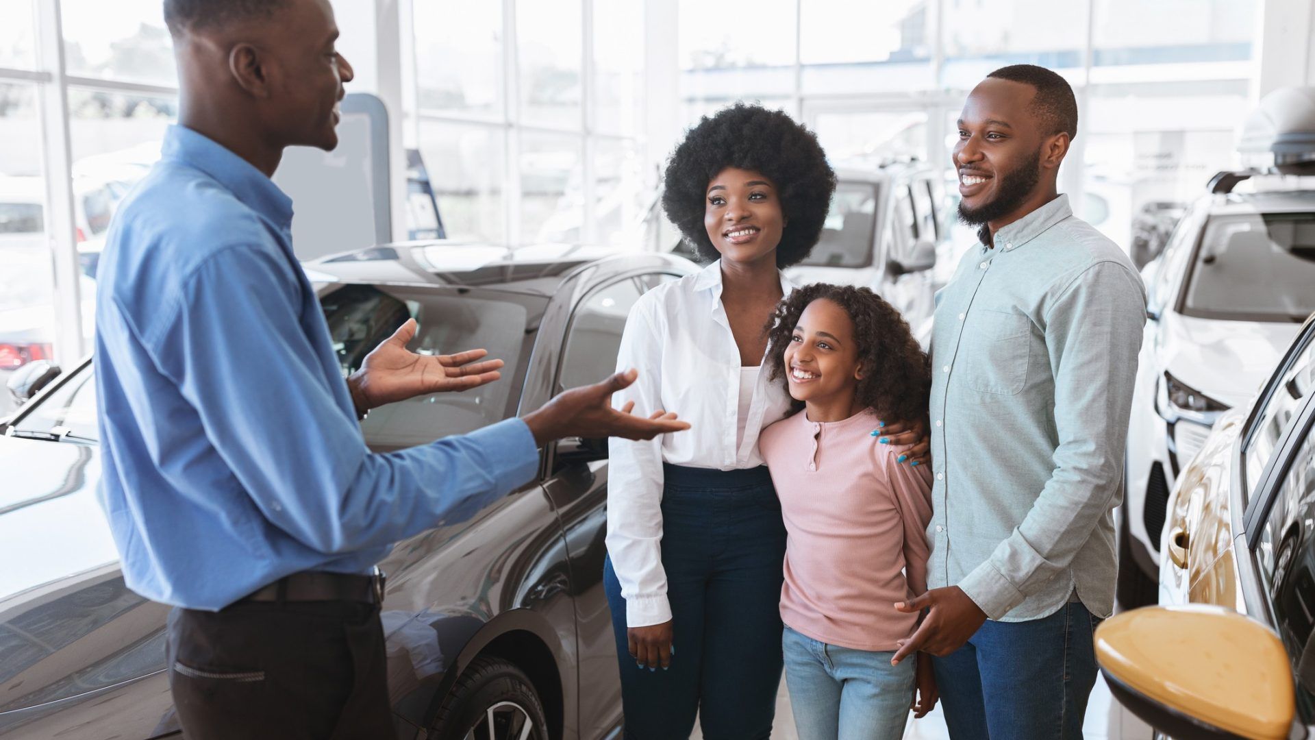 Salesperson showing a car to a smiling family in a bright dealership showroom
