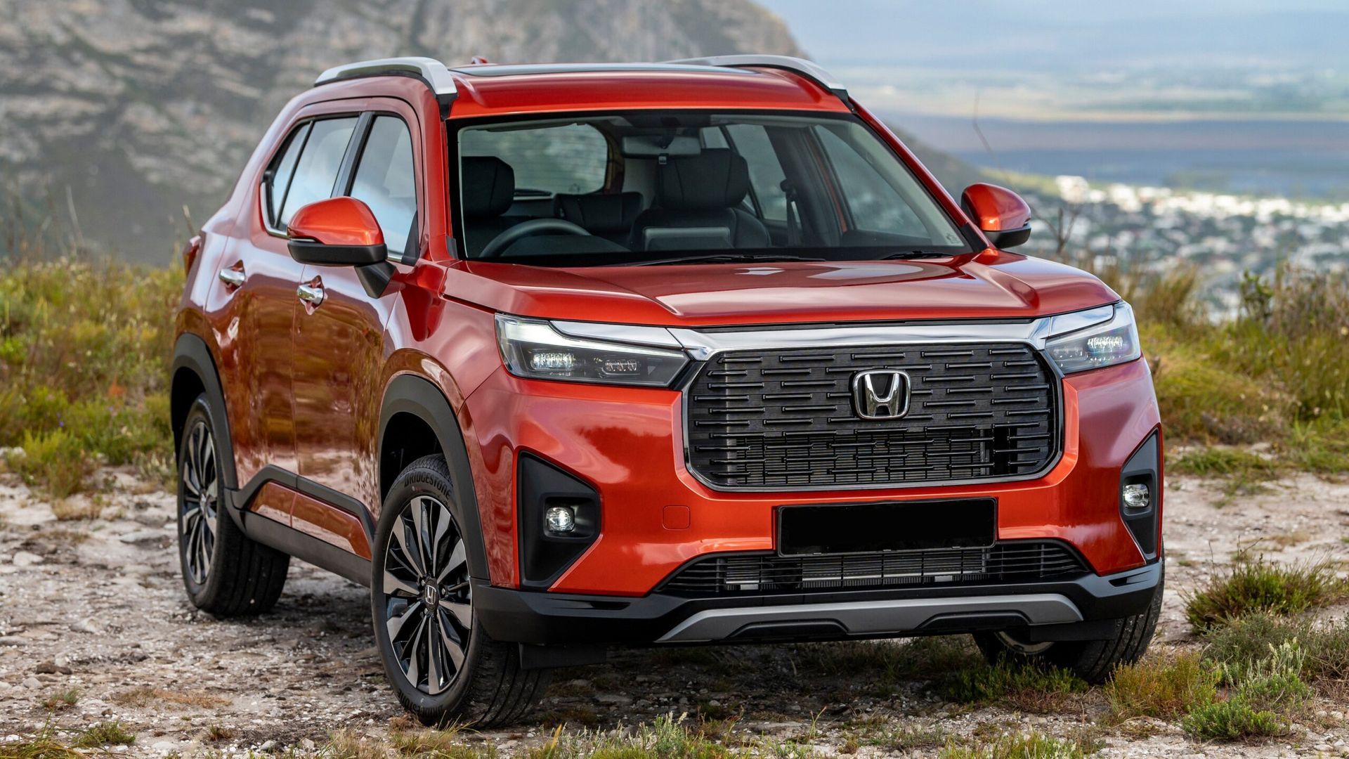 Red Honda SUV parked on a grassy overlook with a cityscape in the background
