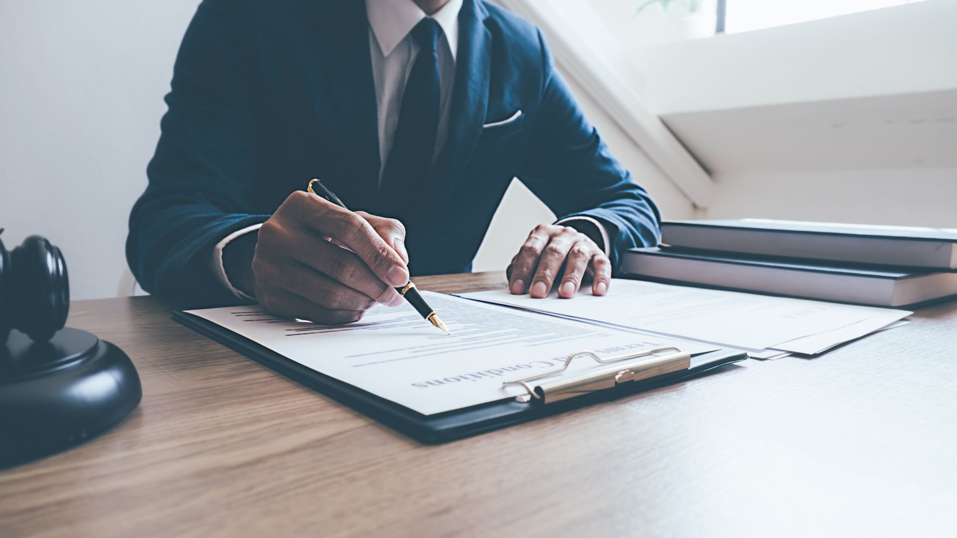 Person in a suit signing papers at a desk with a clipboard and coffee cup