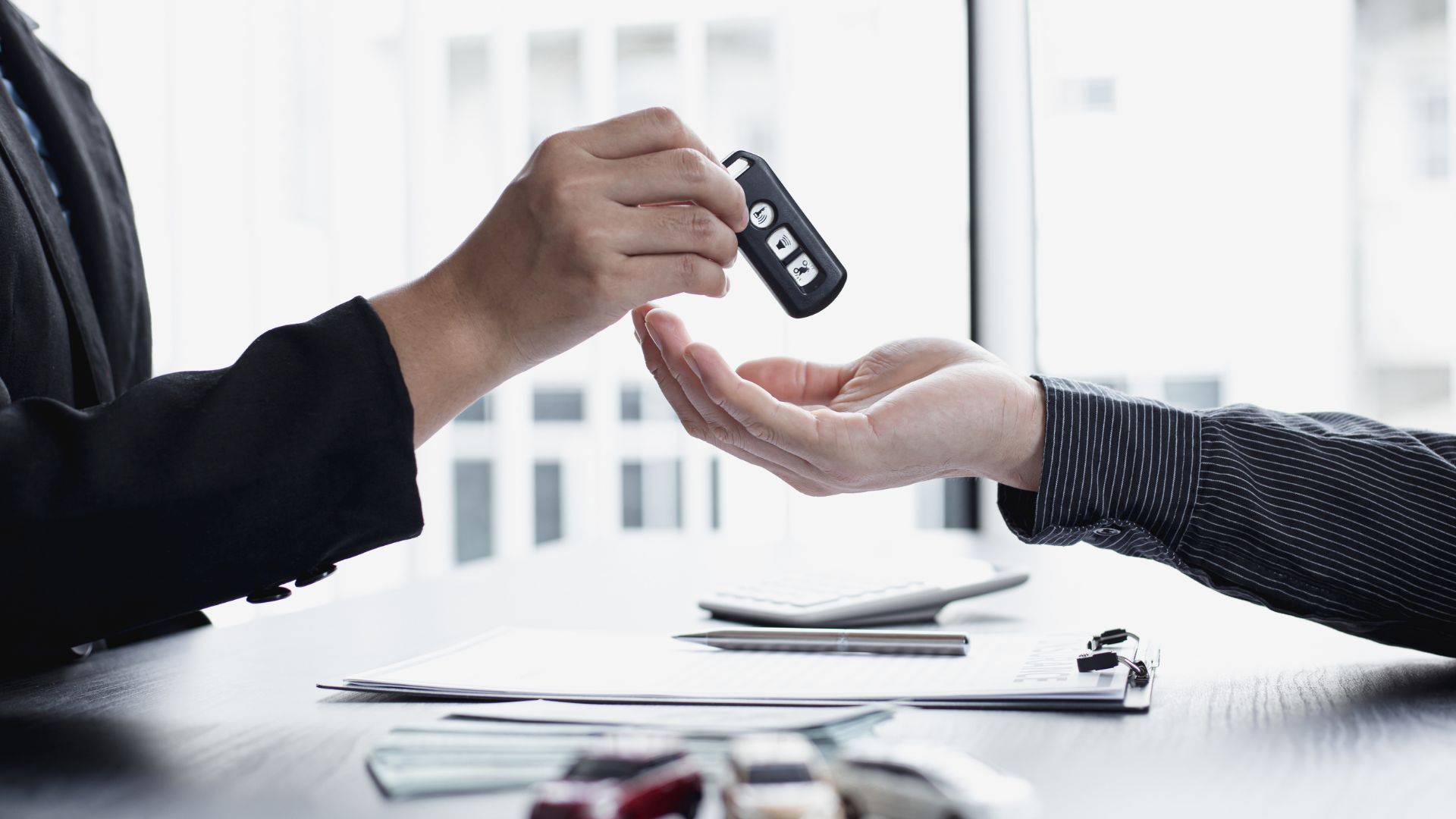Handing over a black car key fob across a desk during a transaction