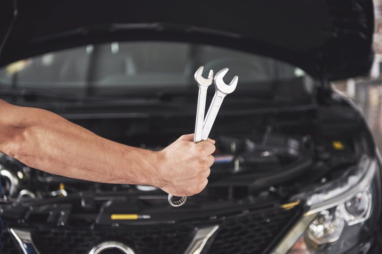 Mechanic holding wrenches in front of a car with the hood open