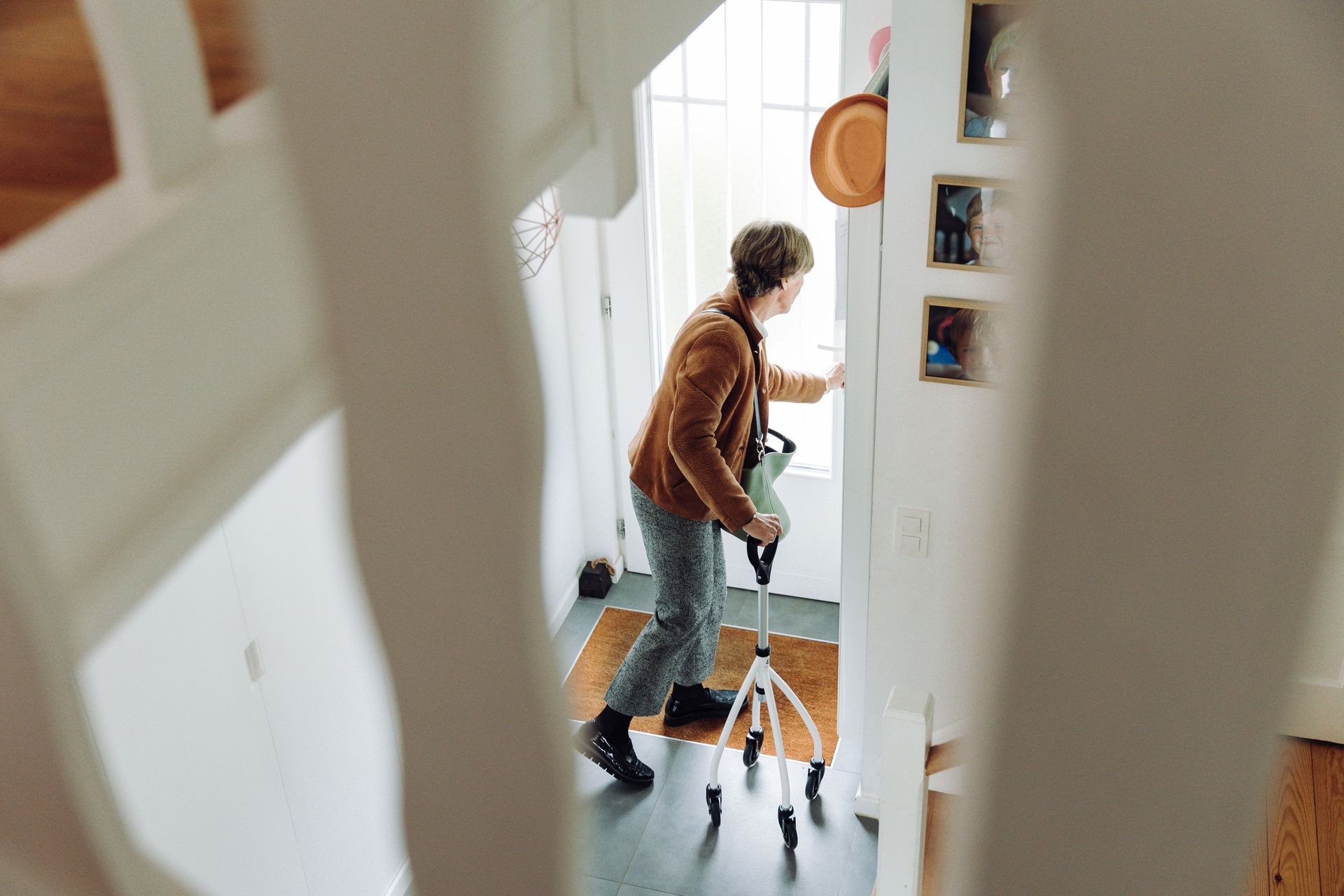 Person walking with a walker in a bright hallway, seen through a doorway.