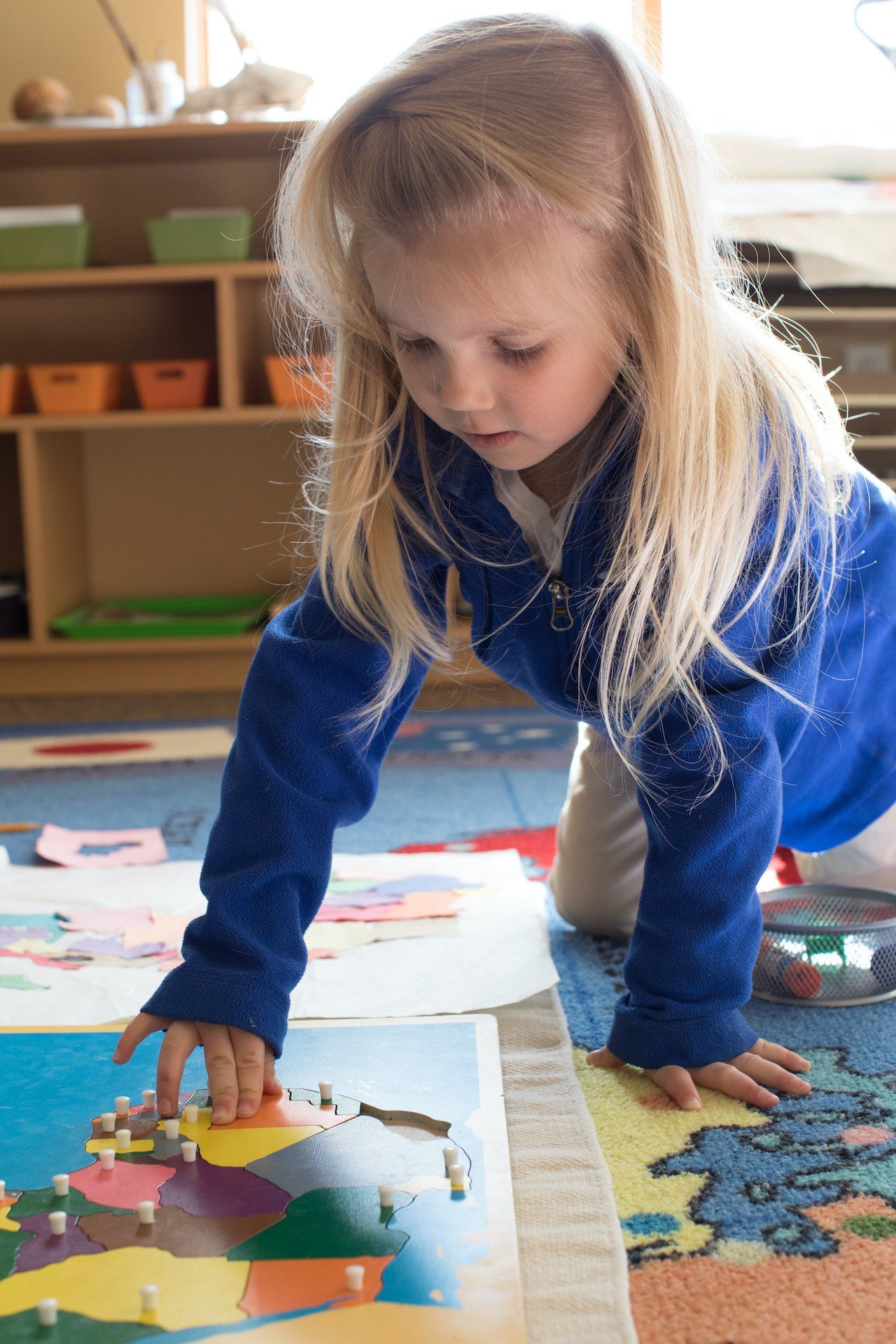 A little girl is working with a wooden montessori map on the floor.