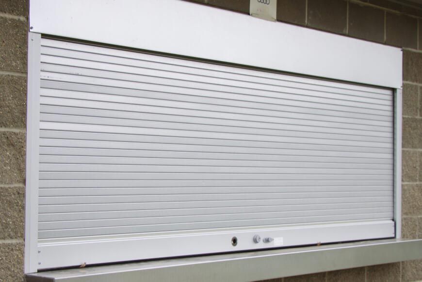 A closed silver metal rolling shutter door installed on a concrete block wall above a counter.