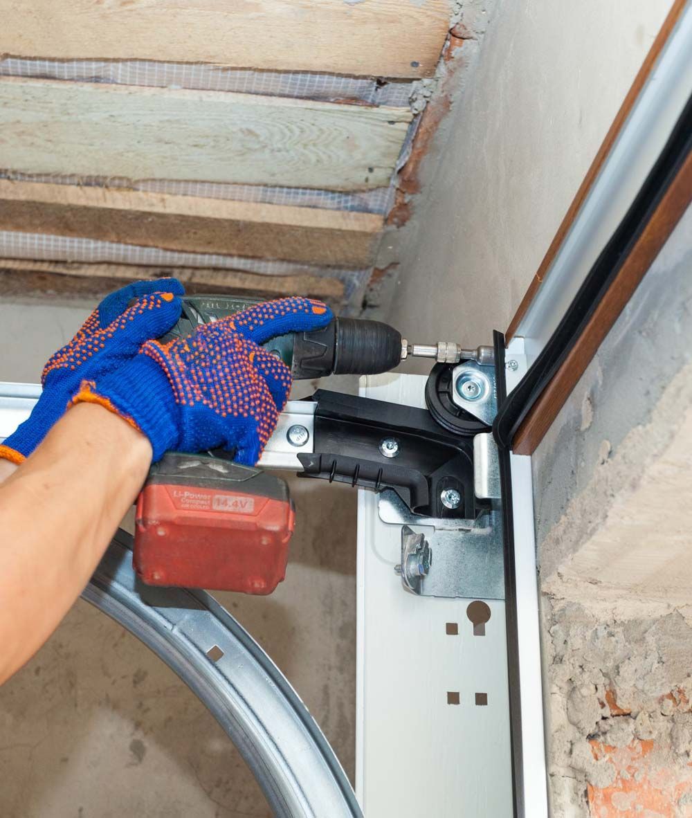 A close-up of a garage door's bottom corner bracket, showing the attached steel cable and roller assembly in a metal track.