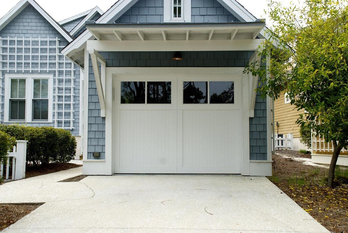 A light blue home with a white garage door, featuring a white pergola over the entrance and a concrete driveway.