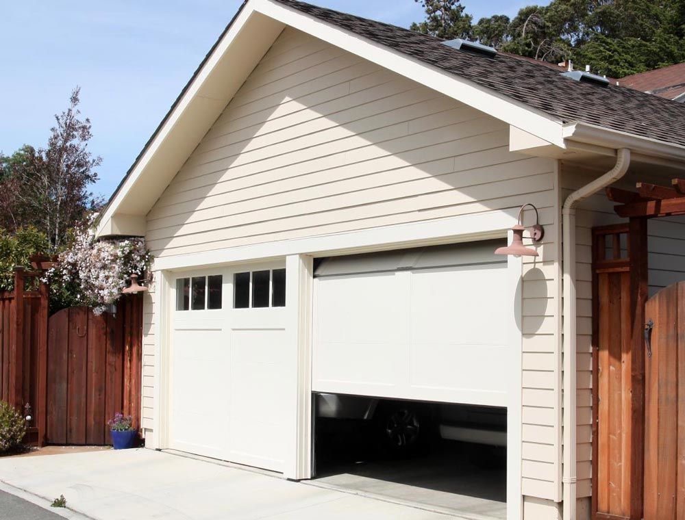 A two-car garage with cream siding, one closed door and one partially open door, attached to a house with a wooden fence.