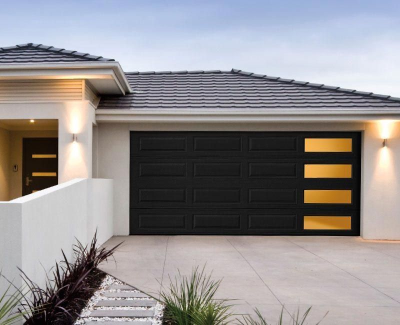 Modern house facade with a dark-colored garage door featuring horizontal windows, light stucco walls, and tiled roof.